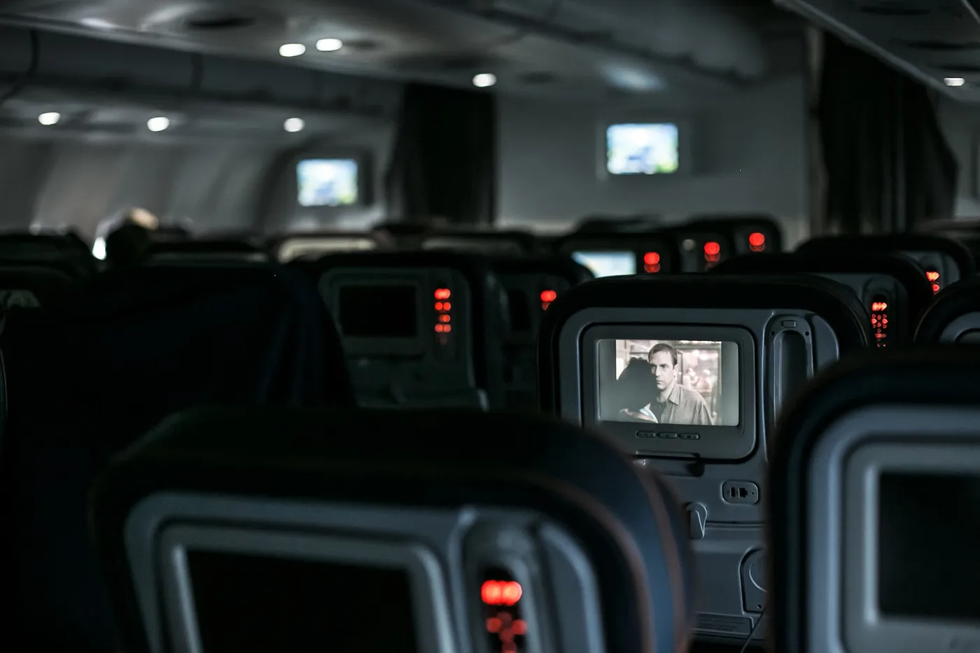Cabine d’avion de nuit : sièges éteints, écrans allumés et feux de rappel ambrés.
